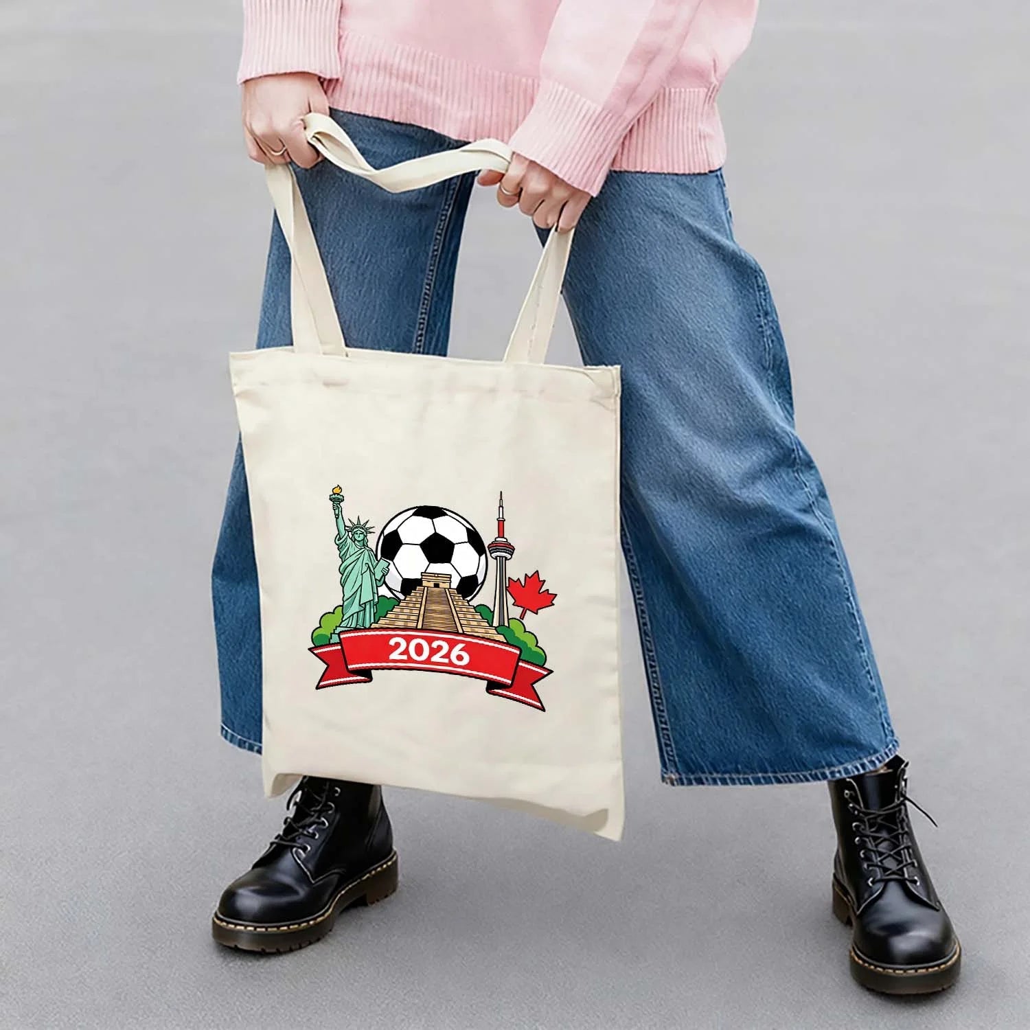 Model carrying 2026 World Cup themed tote bag with USA Statue of Liberty, Mexico pyramid, Canada CN Tower and soccer ball design, cotton canvas bag