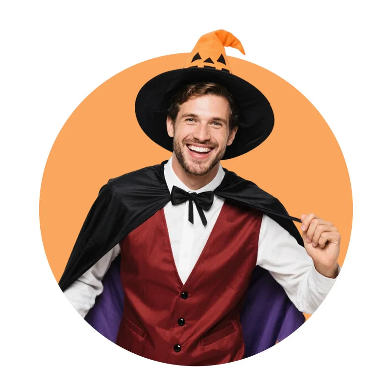 Man in a black/orange pumpkin-shaped Halloween witch hat, red vest, and black cape, set against an orange background.