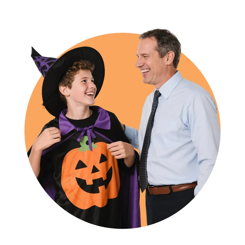Father and son—son in a black Halloween costume with a pumpkin design and witch hat—set against an orange background